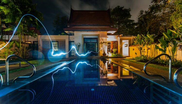 reflection of blue light crossing above pool near house during nighttime